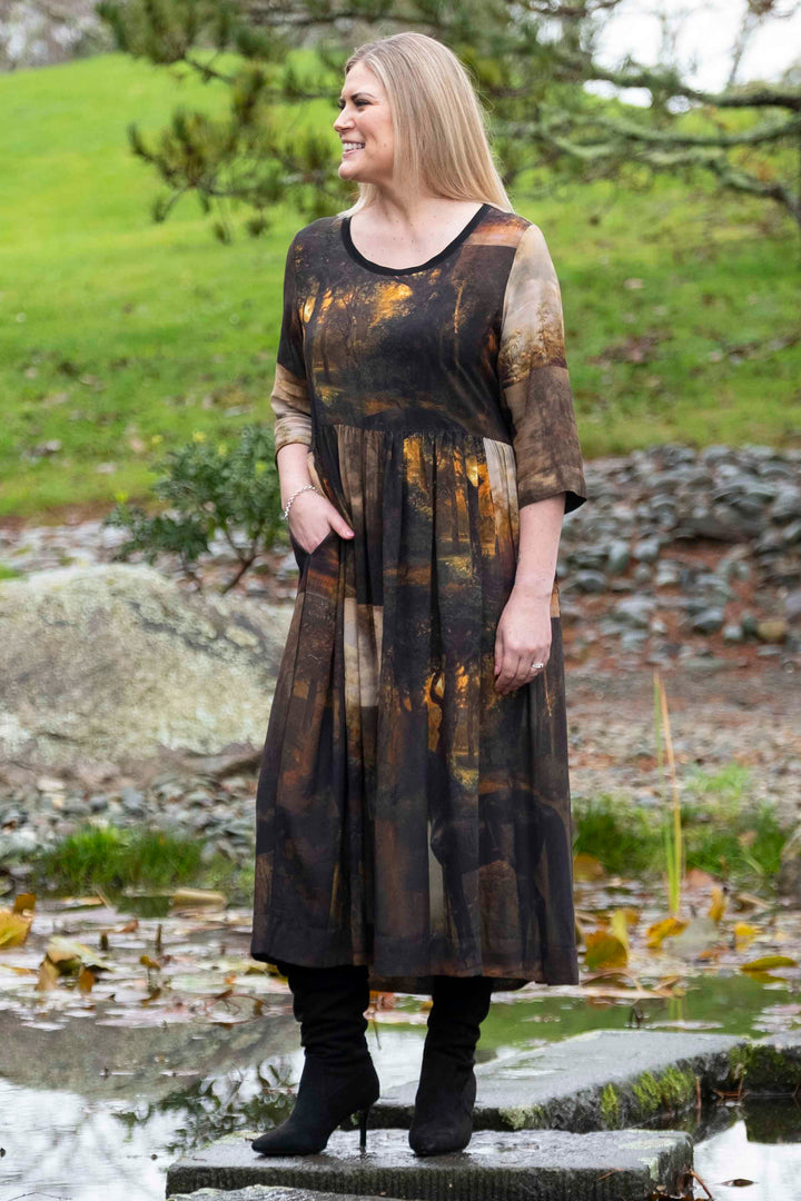 Woman standing by a pond in a long, dark deeanne hobbs tarbana dress with a patterned design created by deeanne hobbs, nz artist.