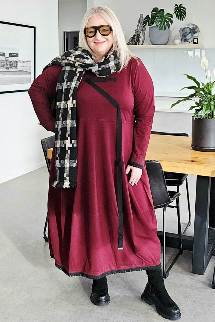 Woman in a burgundy dress with a black and white scarf standing in a modern kitchen.