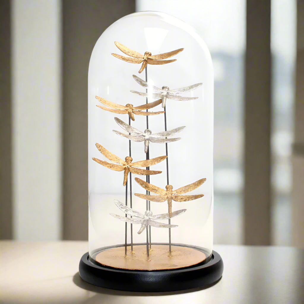 Decorative display of gold and silver dragonflies under a glass dome on a white background