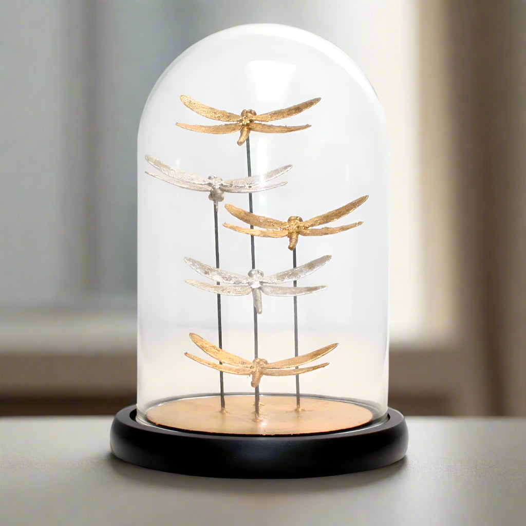Decorative glass dome with gold and silver dragonfly figurines on a white background