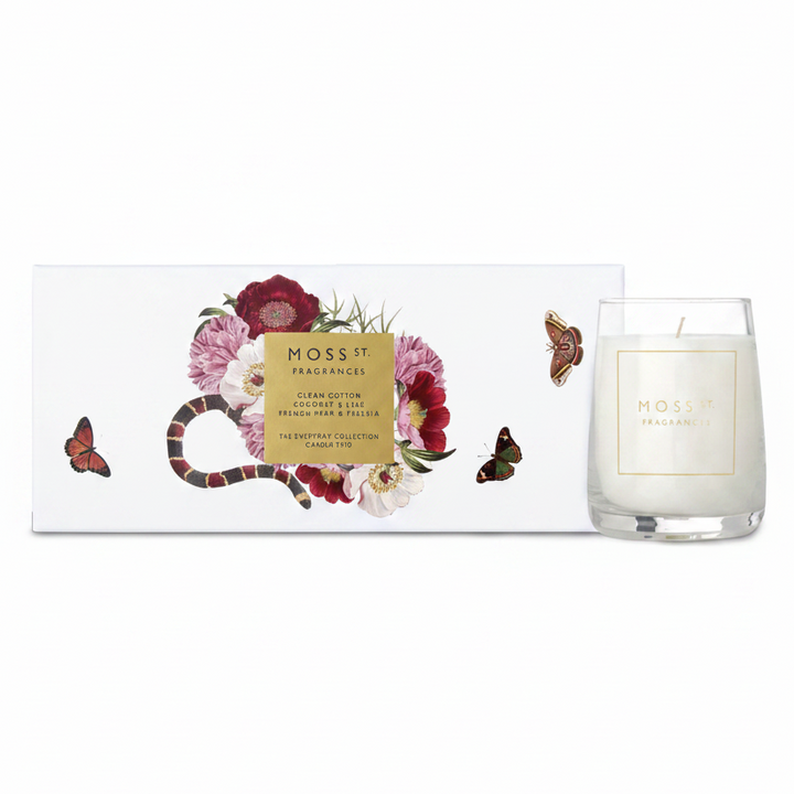 A white scented candle in a clear glass jar sits beside its white box packaging. The box features an illustration of a red and black banded snake wrapped through pink and burgundy flowers, with a central gold label reading 'MOSS ST.
