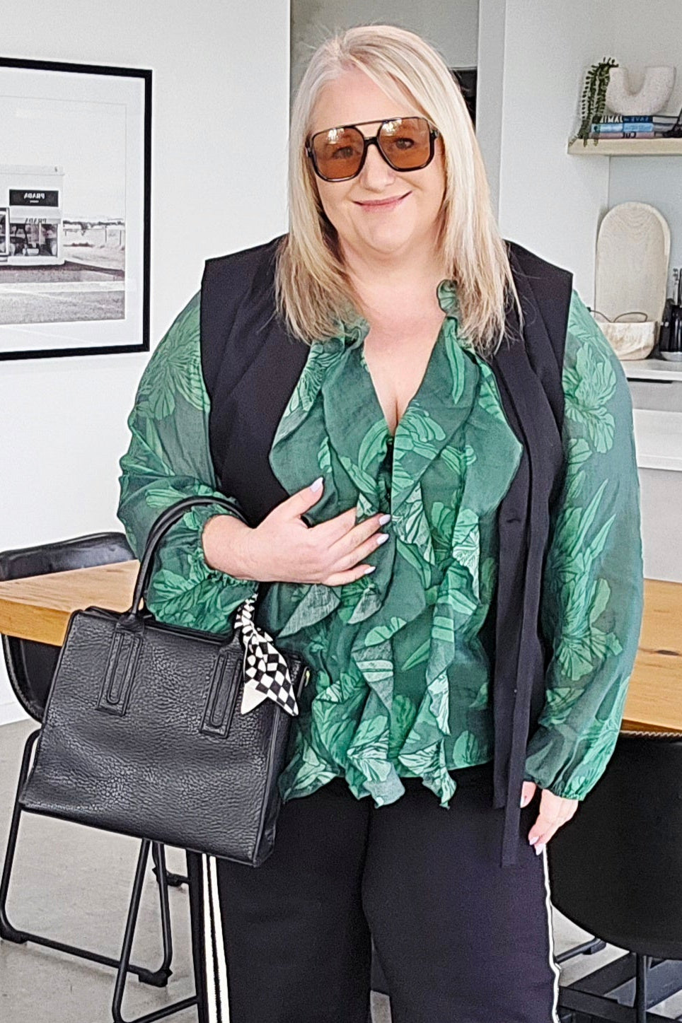 Woman in a stylish outfit with a green top and black pants in an indoor setting.