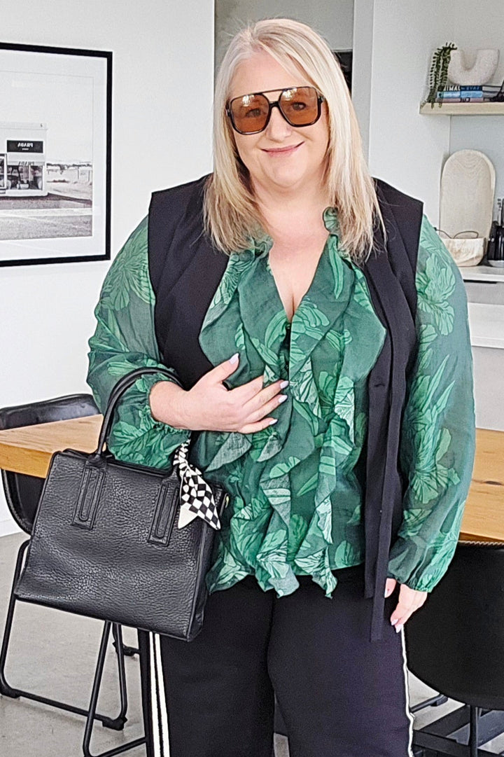 Woman in a stylish outfit with a green top and black pants in an indoor setting.