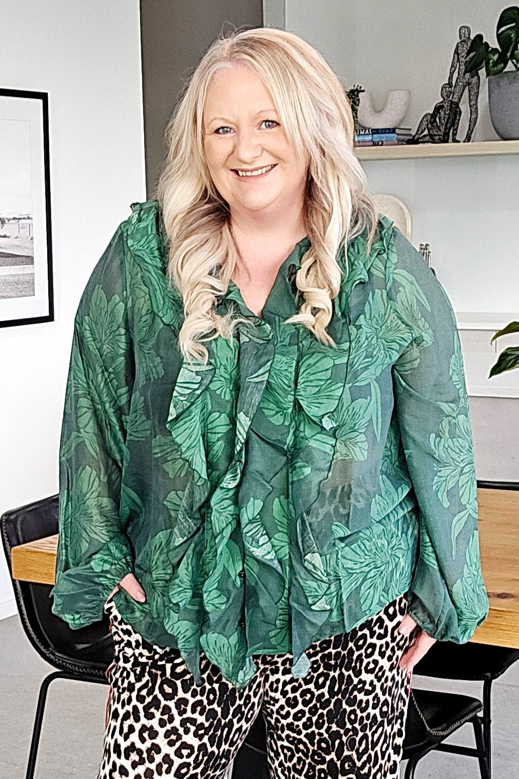 Woman wearing a green patterned top and leopard print pants in an indoor setting.