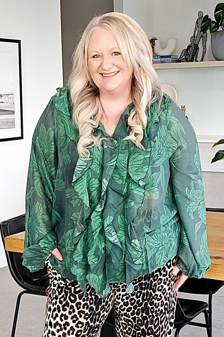 Woman wearing a green patterned top and leopard print pants in an indoor setting.