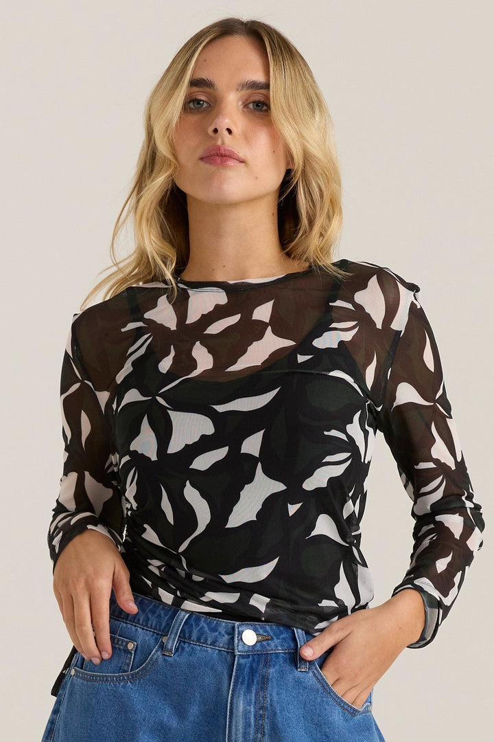 Woman wearing a FATE & BECKER patterned mesh top and blue jeans against a plain background