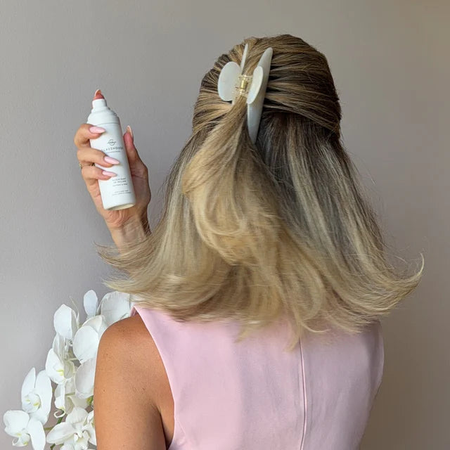 Person with styled hair holding a hair spray bottle against a neutral background
