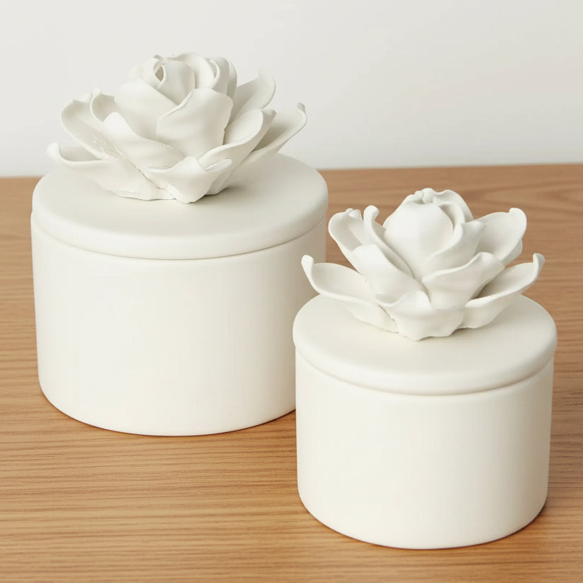 Two matte white porcelain lidded storage jars with sculptural flower-shaped lids, shown on a clean white background.