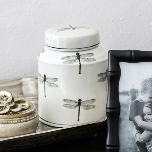 Decorative items including a photo frame with a black bamboo design, a candle with dragonfly design, and a small decorative box on a surface.