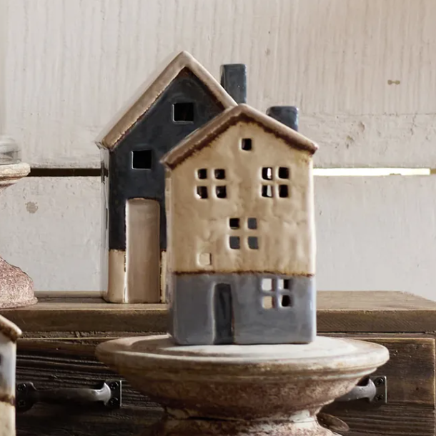 Ceramic house sculpture on a wooden pedestal with a neutral background