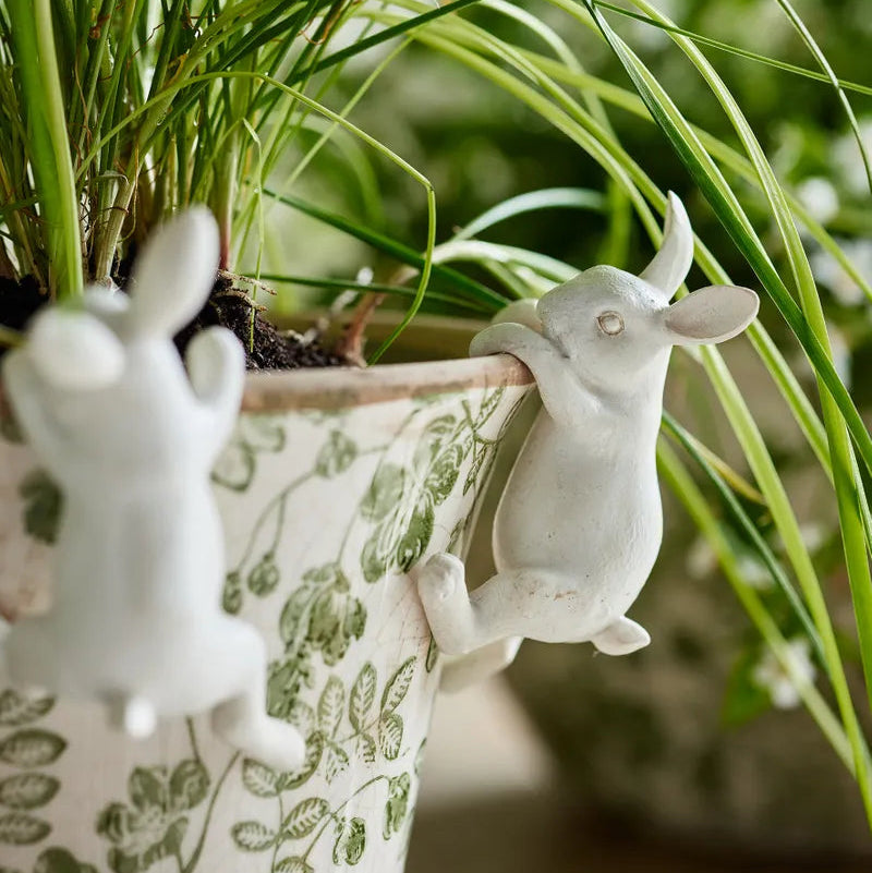 white garden ornament of a white bunny hanging onto the side of a planter pot.
