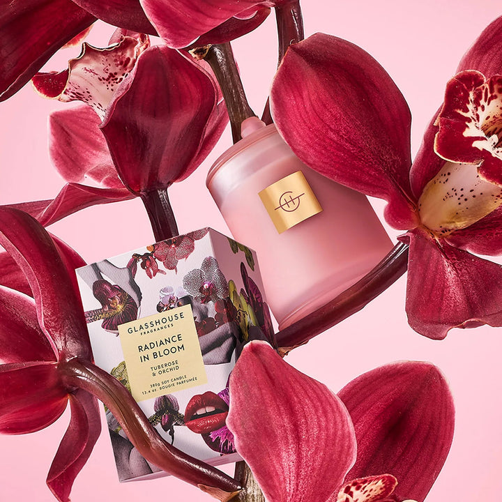 Pink perfume bottle with a gold cap surrounded by red flowers on a pink background