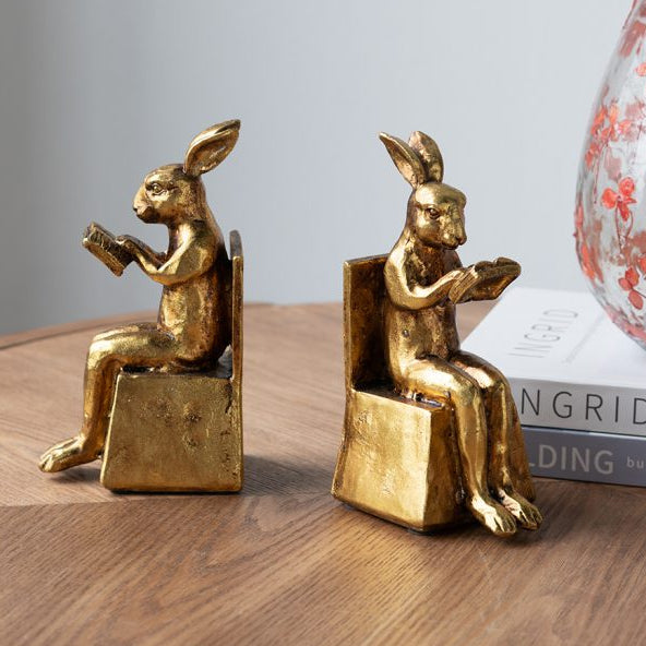 Gold rabbit sculptures on a wooden surface with a light gray background
