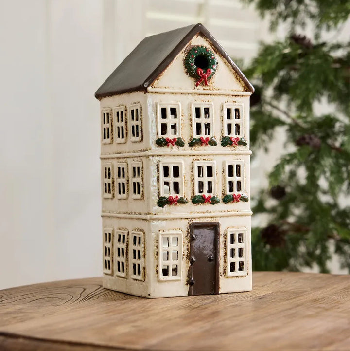 Decorative house-shaped lantern with Christmas wreaths on a wooden surface.