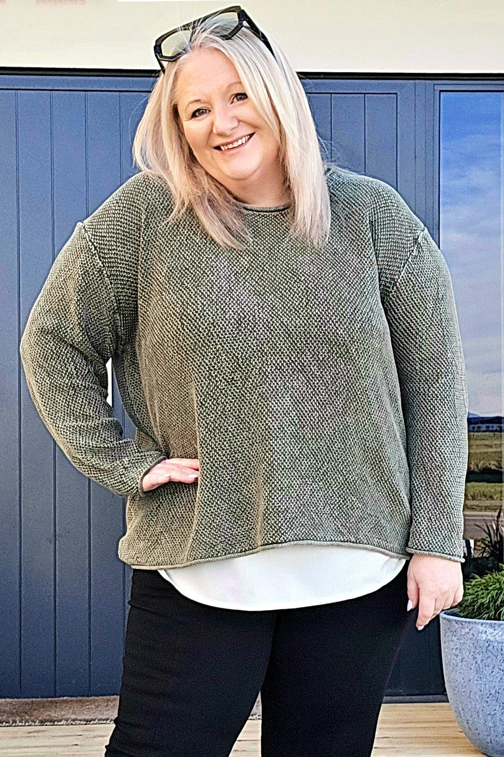 Woman standing outdoors wearing a green sweater, black pants, and white shoes with black bows.