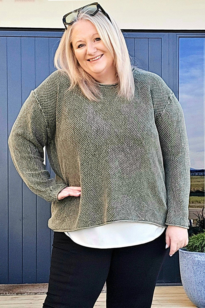 Woman standing outdoors wearing a green sweater, black pants, and white shoes with black bows.