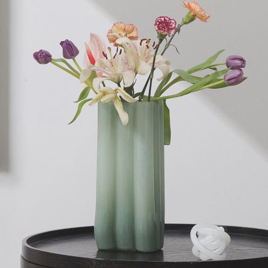Green vase with flowers on a black round table against a white wall