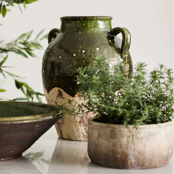 Two ceramic pots on a marble surface with greenery in the background