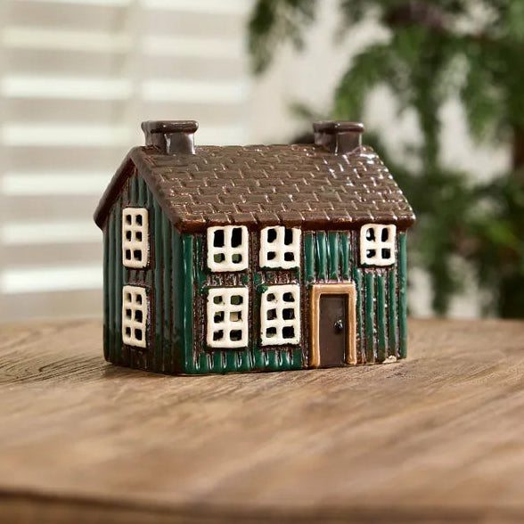 Small model of a house on a wooden surface with a blurred plant in the background
