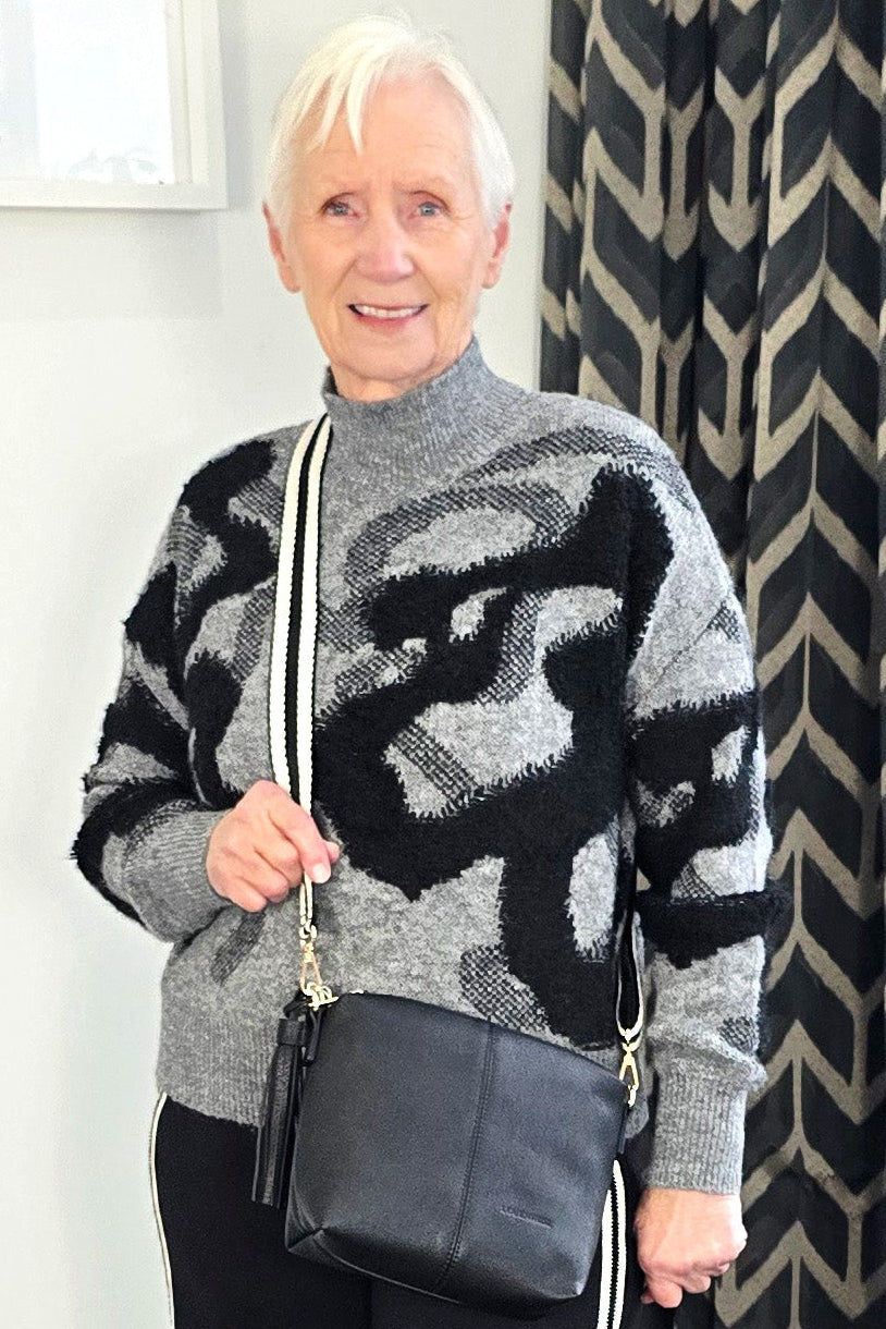 Woman wearing a patterned sweater and black pants with white stripes indoors.