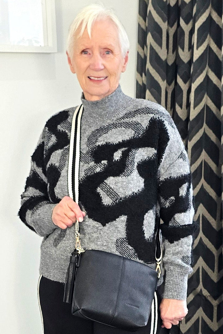 Woman wearing a patterned sweater and black pants with white stripes indoors.