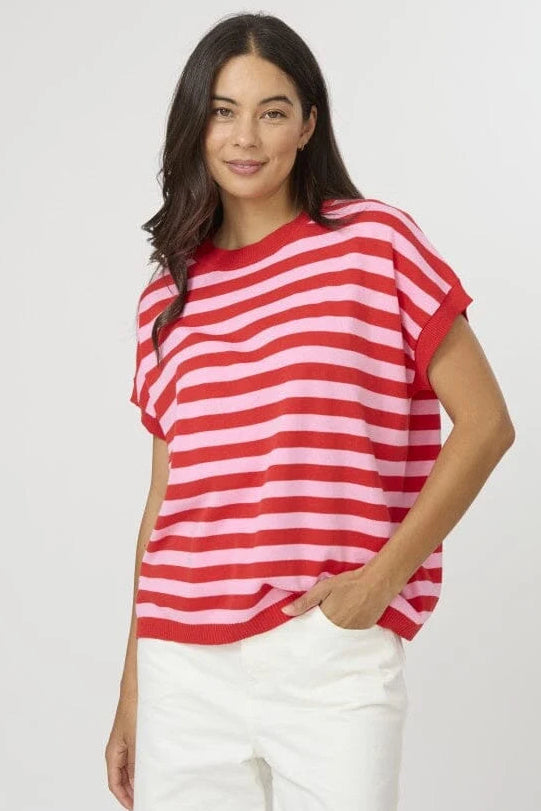 A woman modeling a red and white horizontally striped short-sleeve t-shirt with white pants, standing against a light gray studio background.