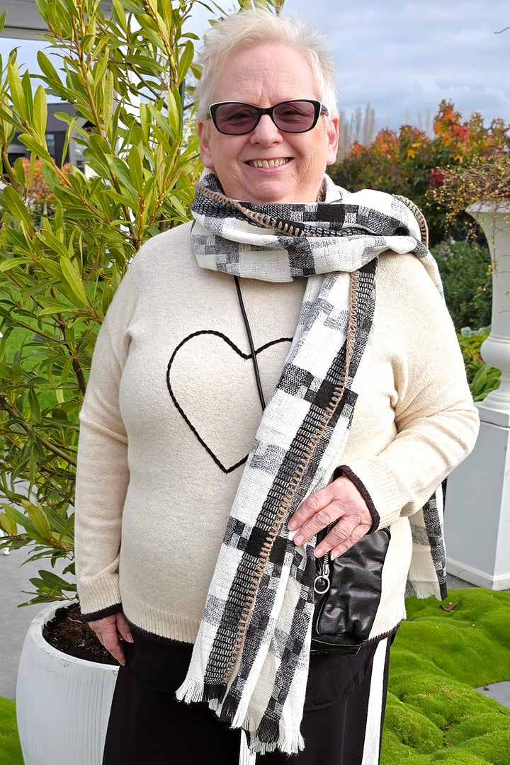 Woman standing outdoors wearing a beige sweater, black pants, and a patterned scarf.