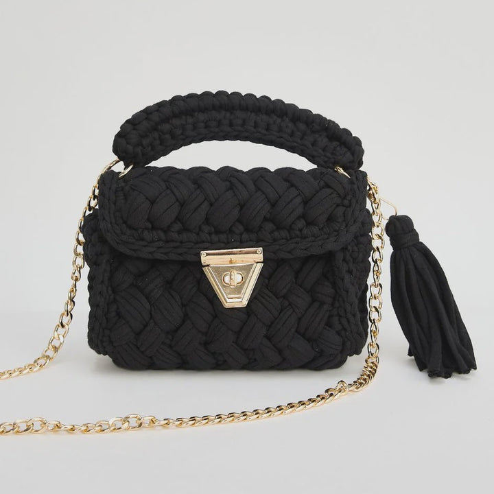 Black woven handbag with a gold chain and tassel on a white background