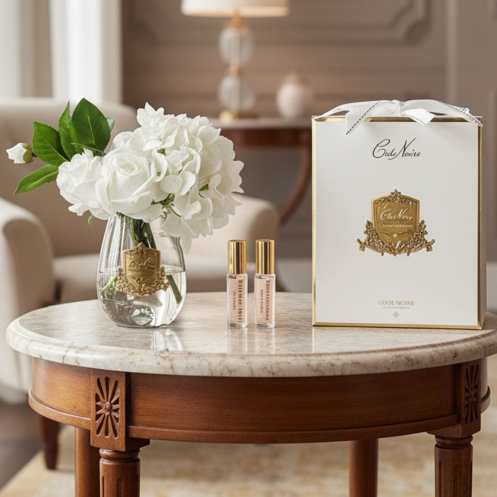 Set with a vase of Cote Noire roses & hyfrangeas in white, two perfume bottles, and a branded box in a luxury room.