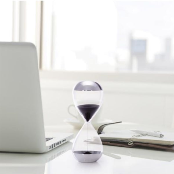 Hourglass on a desk with a laptop and notebook in a blurred office setting