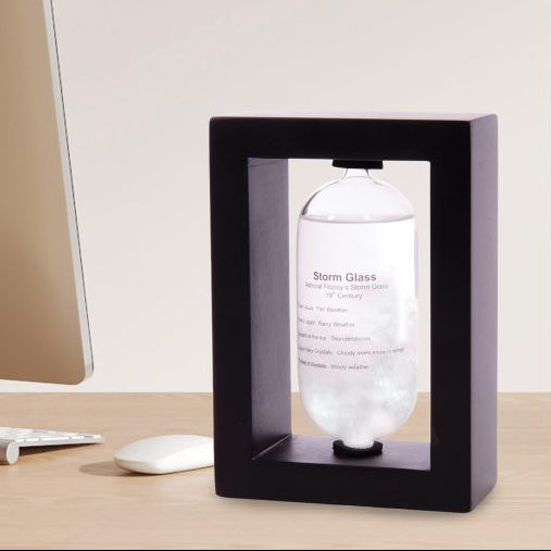Clear glass bottle with label inside a black frame on a desk.