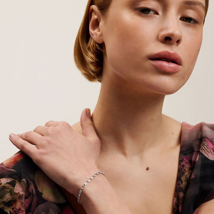Woman wearing a silver ted baker bracelet on a neutral background