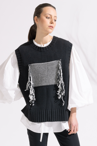 Person wearing a black and white outfit with a patterned sweater on a white background