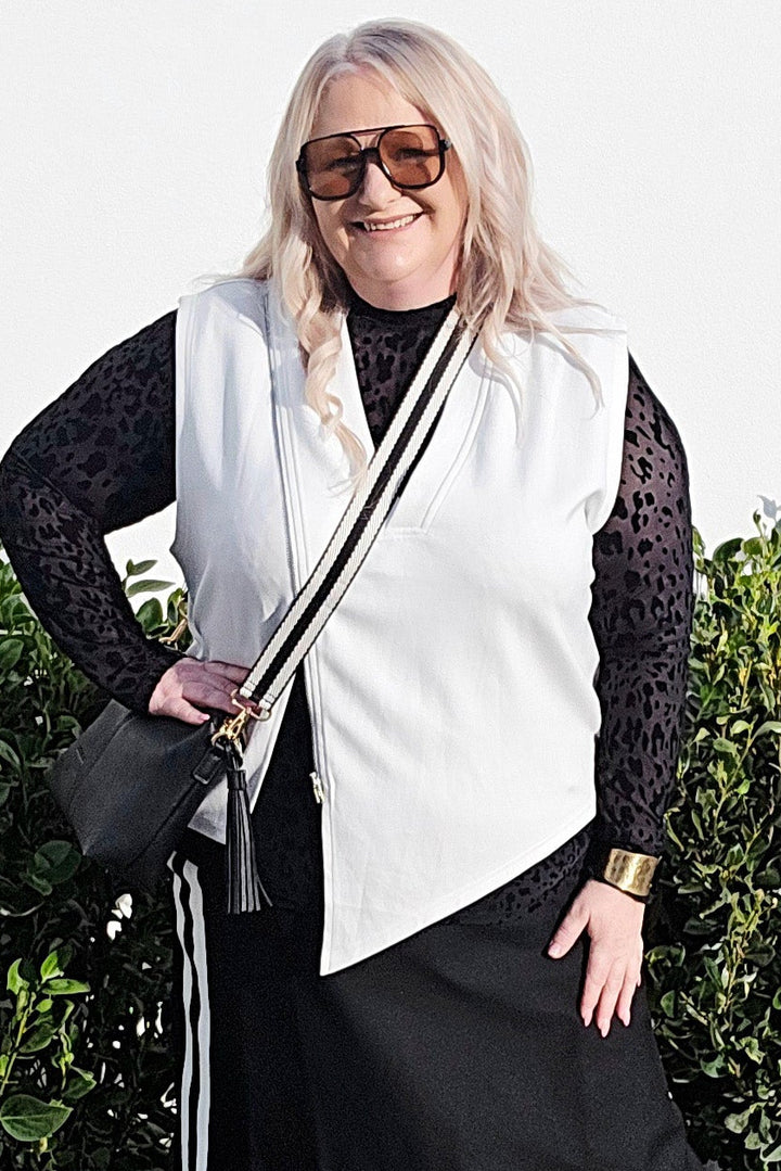 Woman in a black and white outfit standing outdoors with greenery in the background