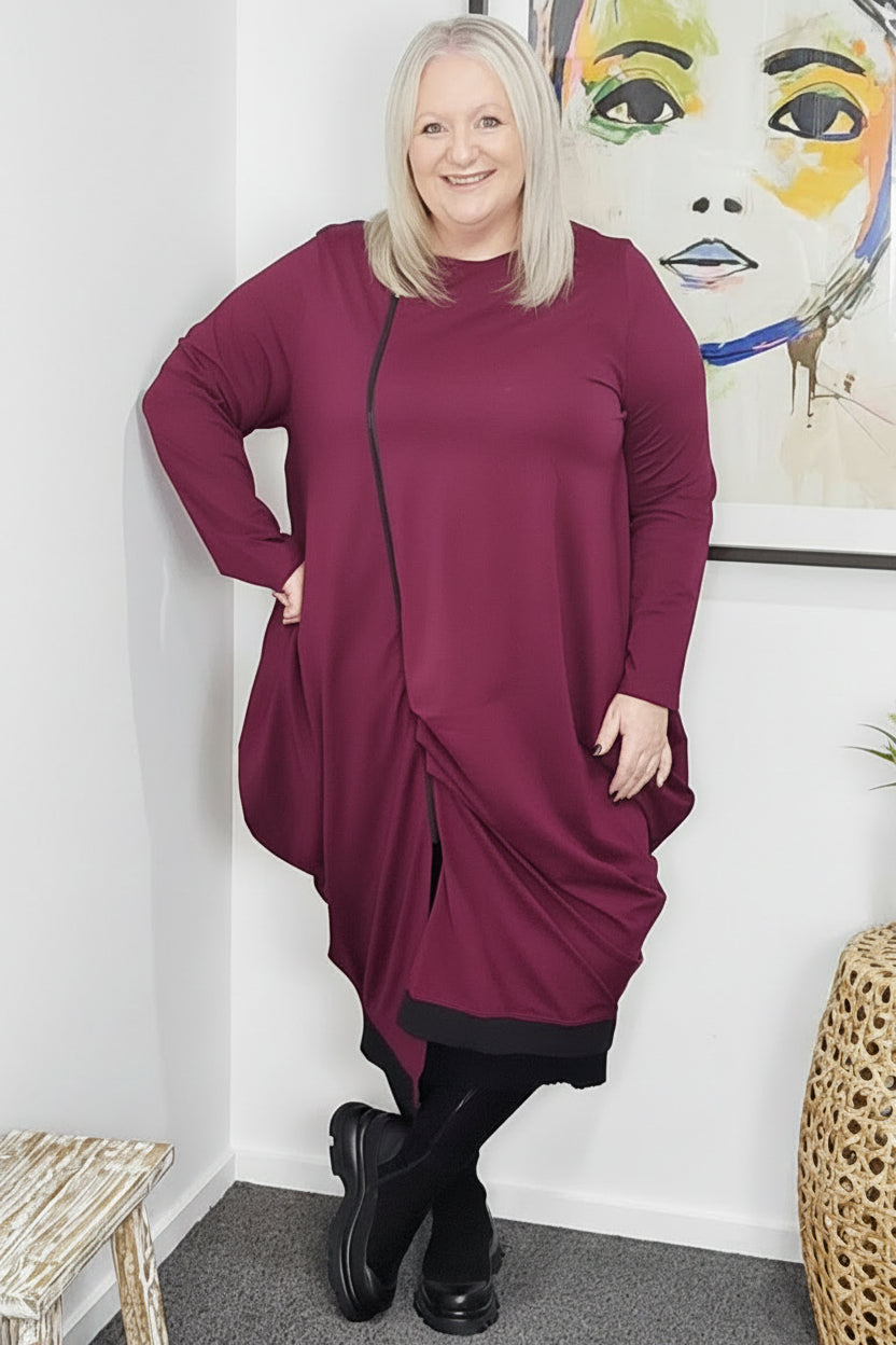 Woman wearing a burgundy dress standing in a room with a colorful abstract painting on the wall.