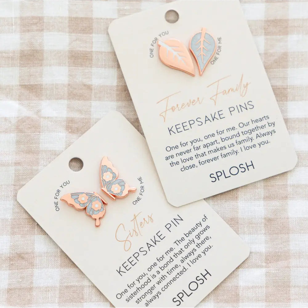 Two keepsake pins with butterfly designs on cards labeled 'Forever Family' and 'SPLASH' on a checkered background.