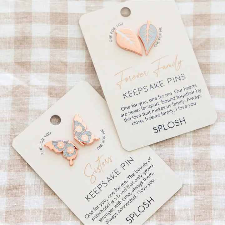 Two keepsake pins with butterfly designs on cards labeled 'Forever Family' and 'SPLASH' on a checkered background.