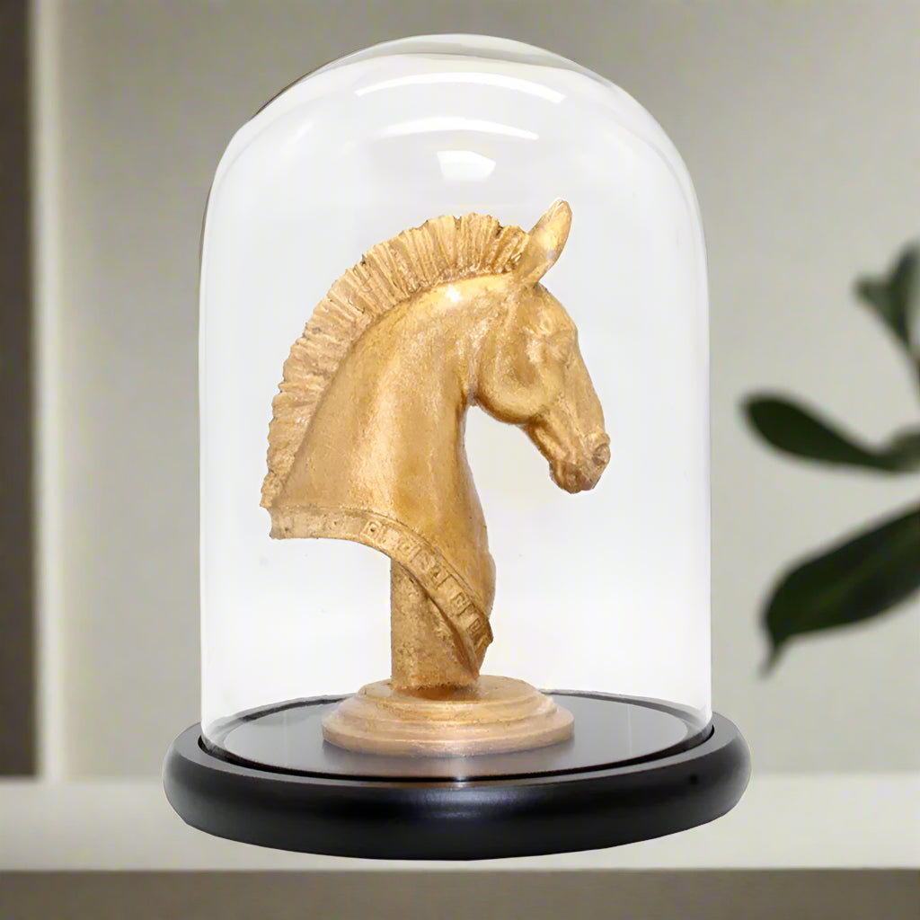 Gold horse head sculpture inside a glass dome on a white background