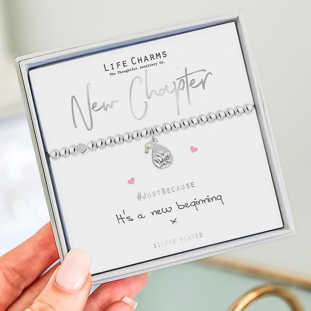 Silver bracelet with a heart charm on a 'Life Charms' card held by a hand.