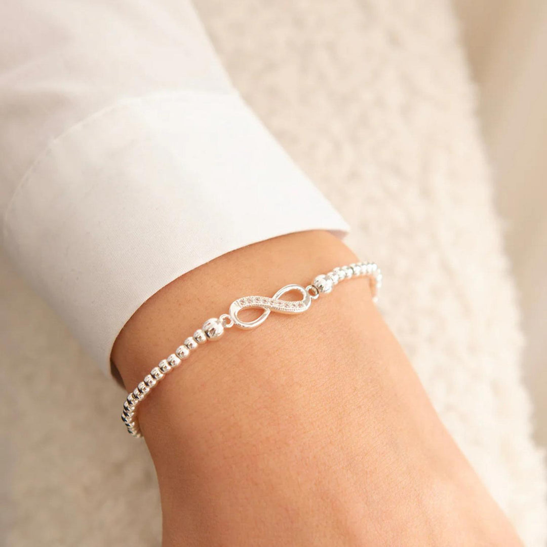 Silver bracelet with infinity symbol on a person's wrist against a neutral background