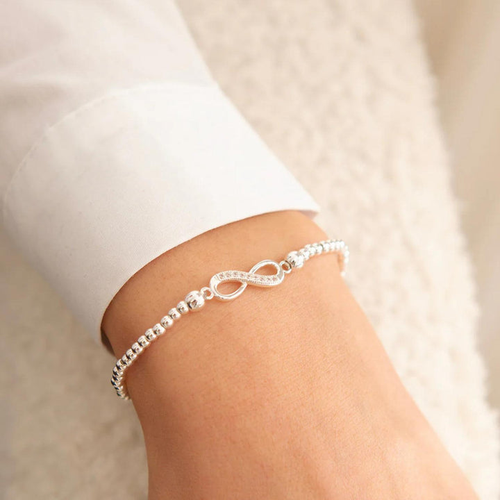 Silver bracelet with infinity symbol on a person's wrist against a neutral background
