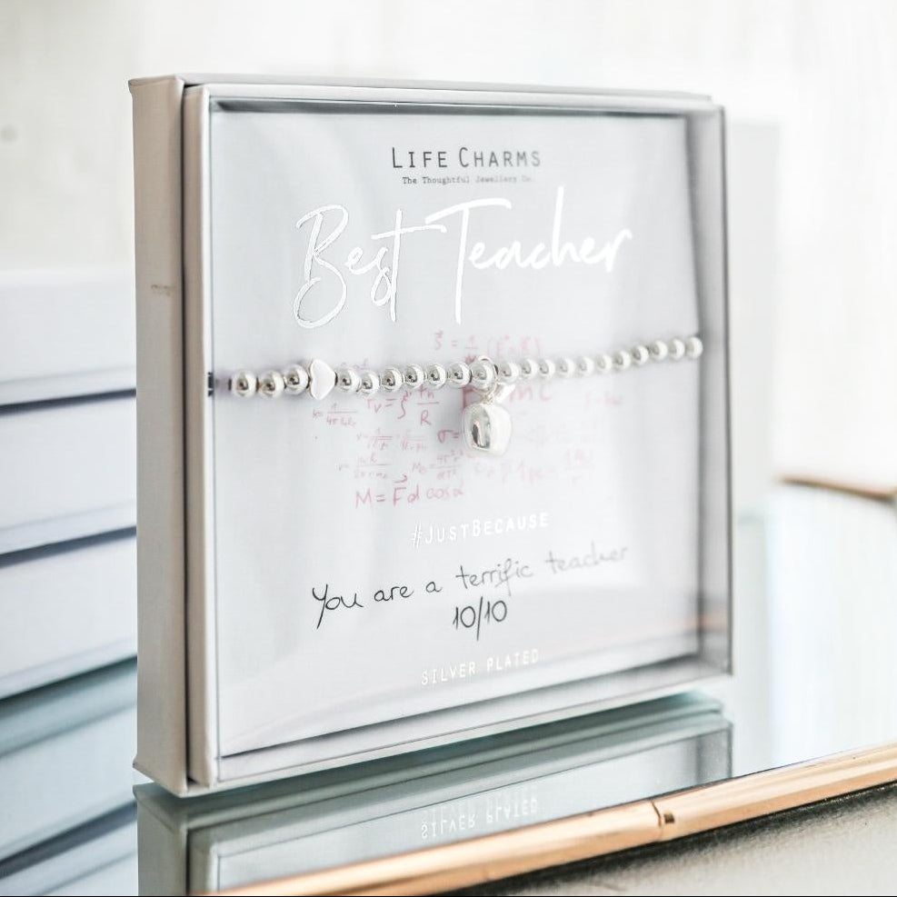 Bracelet in a clear display case with 'Best Teacher' text, flowers in the background