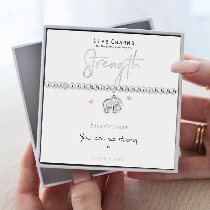 Person holding a card with 'Strength' bracelet design and 'Life Charms' branding.