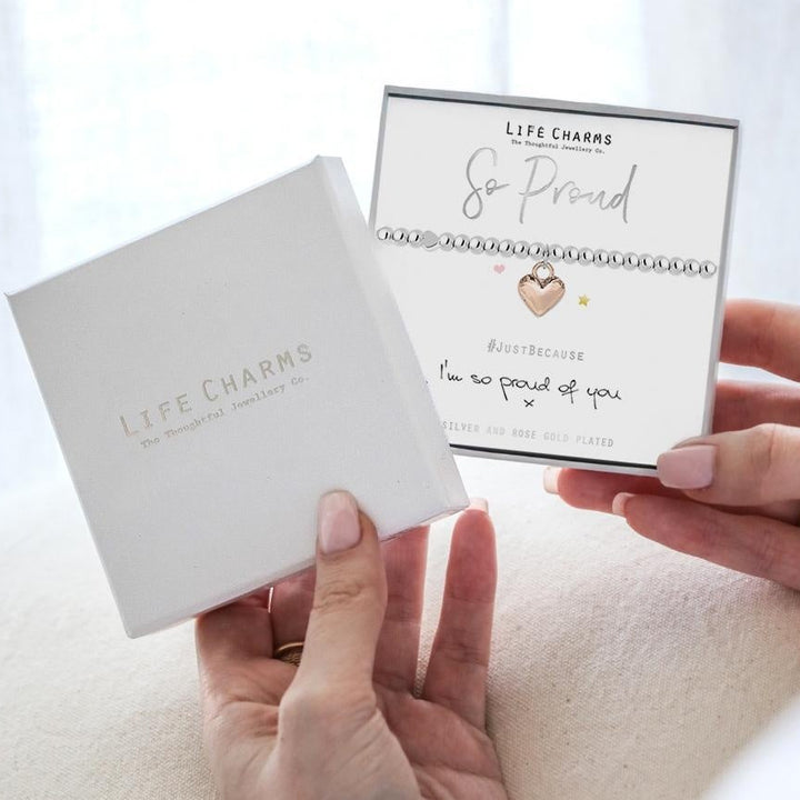 Two hands holding a card and a small box with 'Life Charms' branding against a light background.