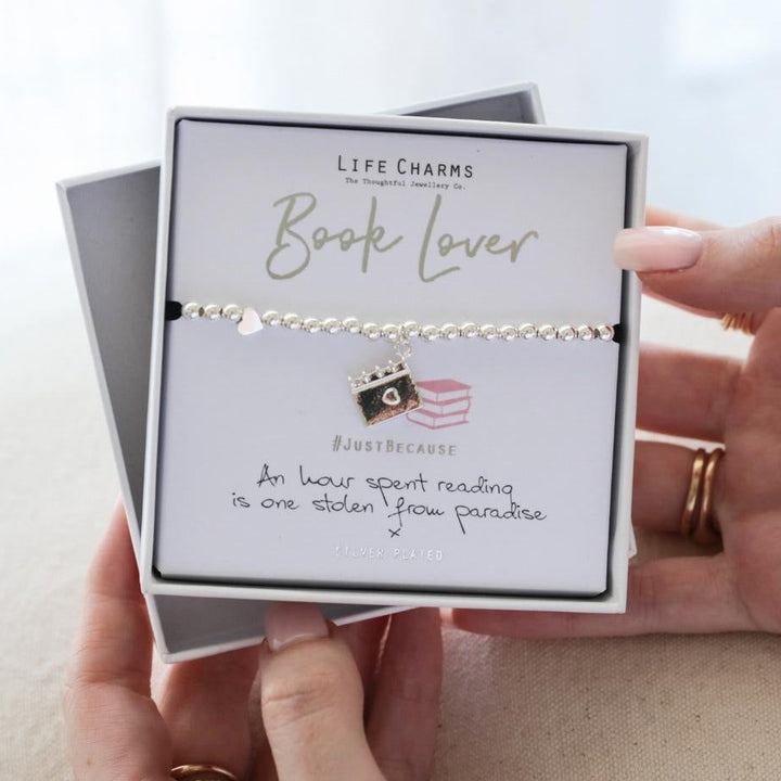 Person holding a 'Book Lover' bracelet in a Life Charms box on a light background