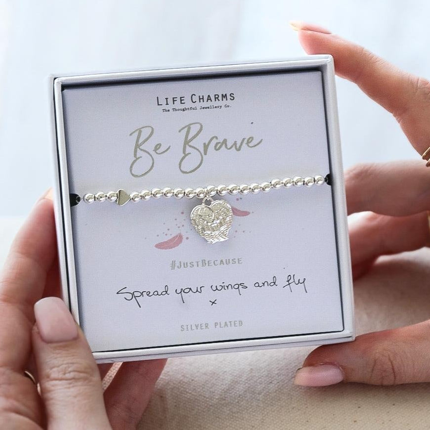 Person holding a box with a 'Be Brave' bracelet and card on a light background
