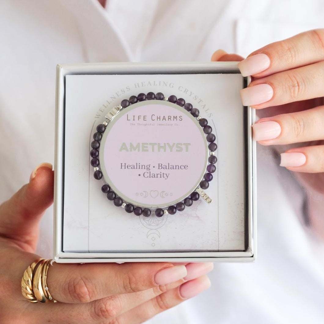 Amethyst bracelet in a box held by a person wearing gold rings.