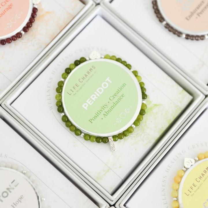 Close-up of a Life Charms bracelet with 'Peridot' on a grid background