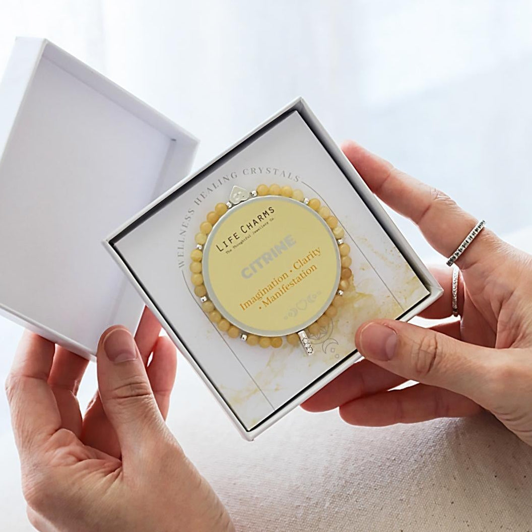 Person holding a small round citrine bracelet in a white box with a white background