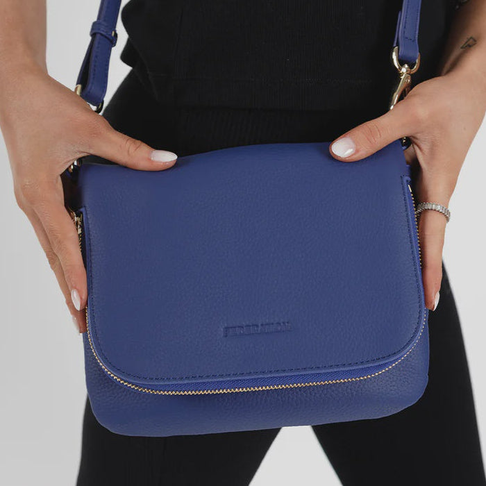 Person holding a blue leather federation crossbody bag against a plain background